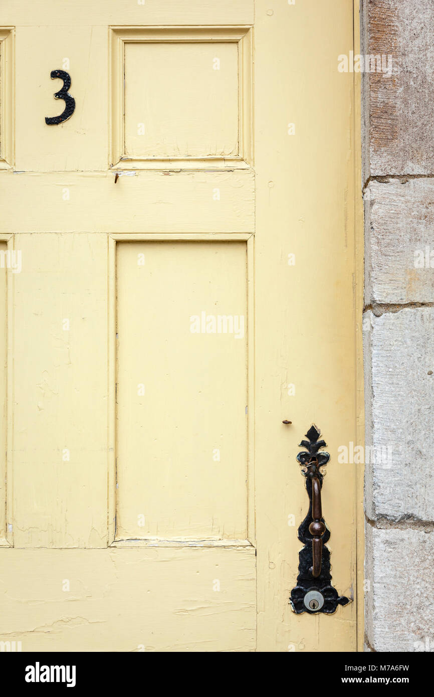 Vecchio di colore giallo pallido con porta porta di antiquariato hardware e un numero tre. Foto Stock