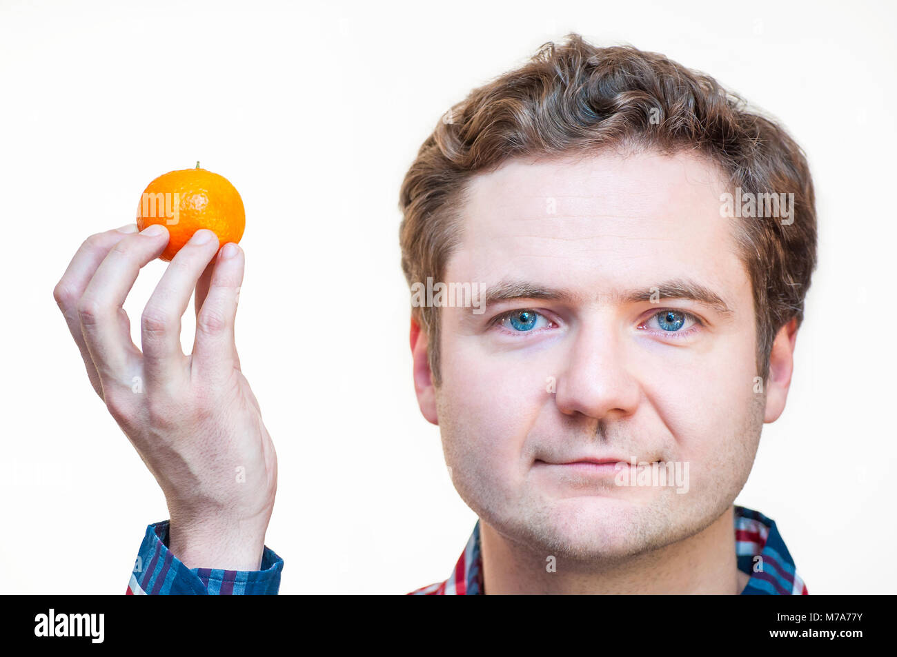 Ritratto di giovane con occhi blu etnia caucasica uomo azienda tangerine nella mano destra vicino alla sua testa su sfondo bianco. Foto Stock