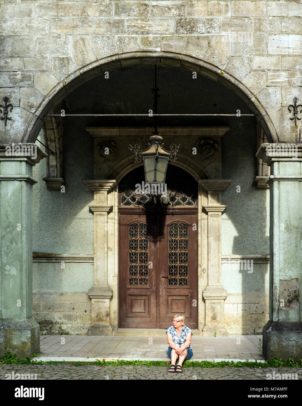 Caucasian donna di mezza età in plaid shirt seduti sulle scale su vintage sfondo della porta Foto Stock