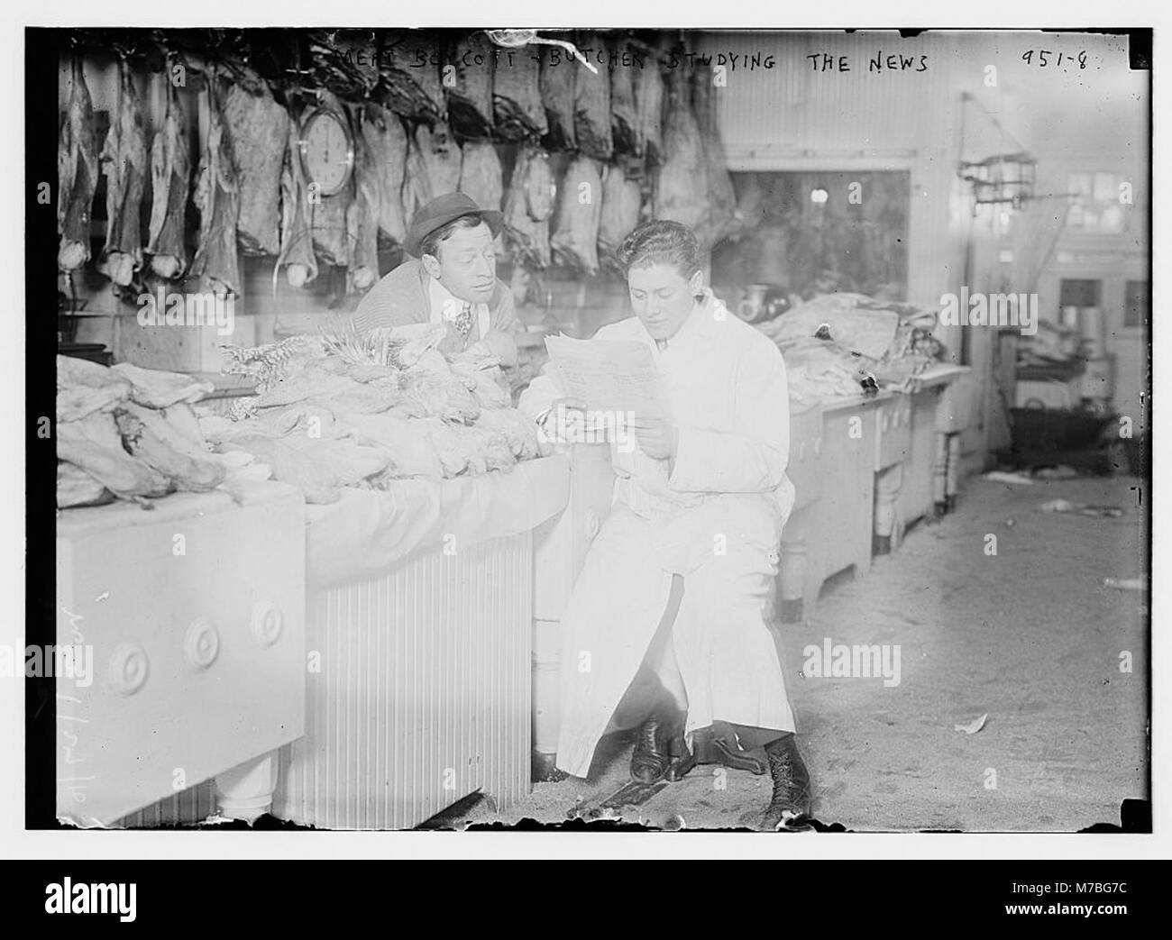 I macellai stanno leggendo i giornali ai loro banchi, che sono pieni di carne, durante un boicottaggio della carne. La fotografia cattura un momento della storia durante la protesta economica sull'aumento dei prezzi della carne. Foto Stock