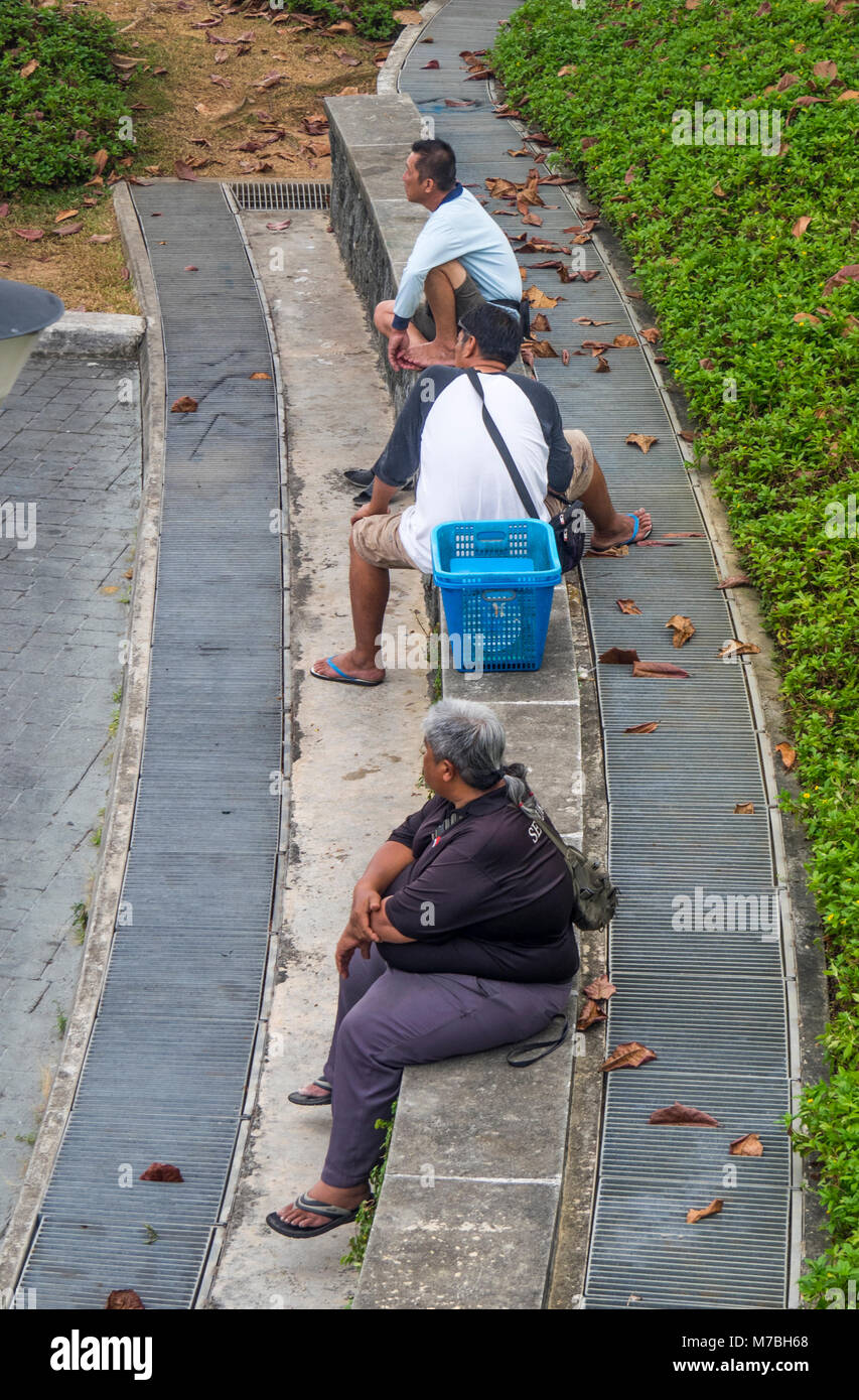 Tre uomini di Singapore seduto su una mensola in attesa. Foto Stock
