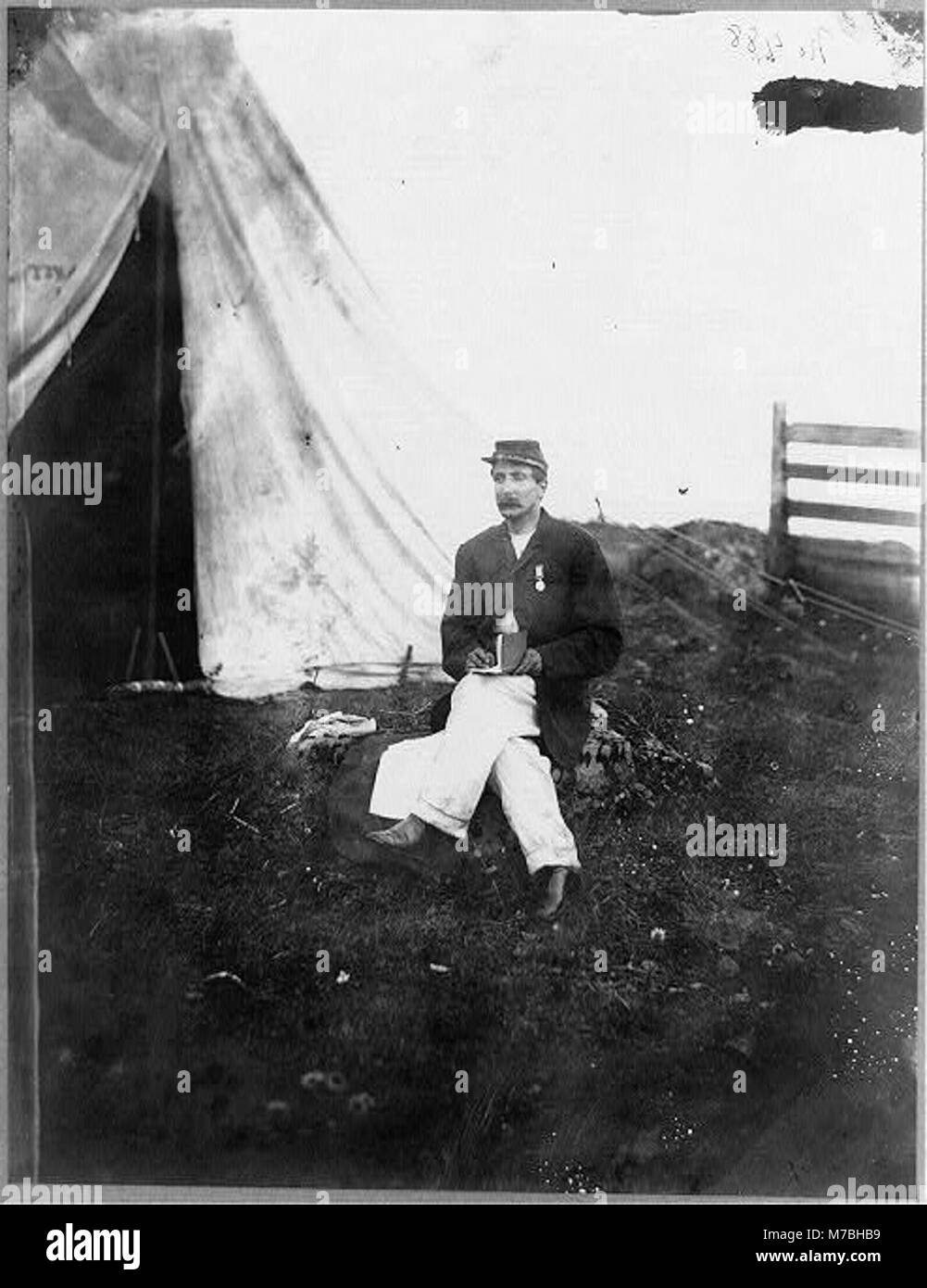 Questo ritratto a figura intera raffigura l'impiegato del capitano Huff seduto di fronte a una tenda, con in mano un libro. L'immagine cattura un momento nella vita militare o amministrativa, mostrando l'abbigliamento e l'ambiente del tempo. Foto Stock