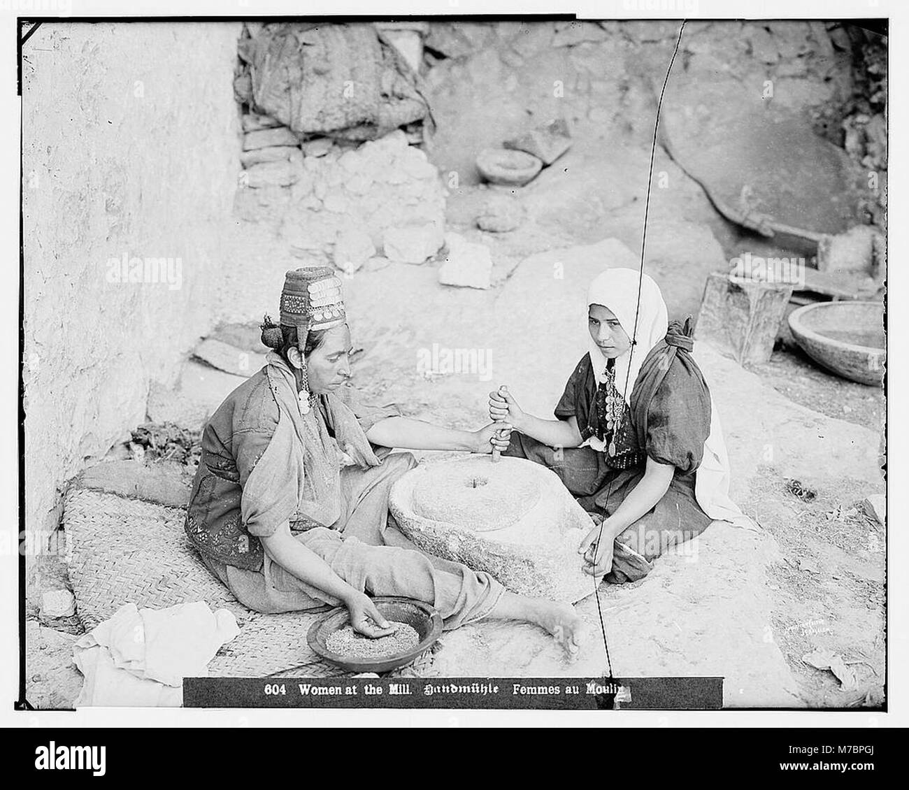 Raffigurazione di due donne che macinano il grano in un mulino, vestite con costumi storici. L'immagine riflette il lavoro quotidiano e i metodi tradizionali utilizzati nella produzione alimentare durante i secoli precedenti. Foto Stock