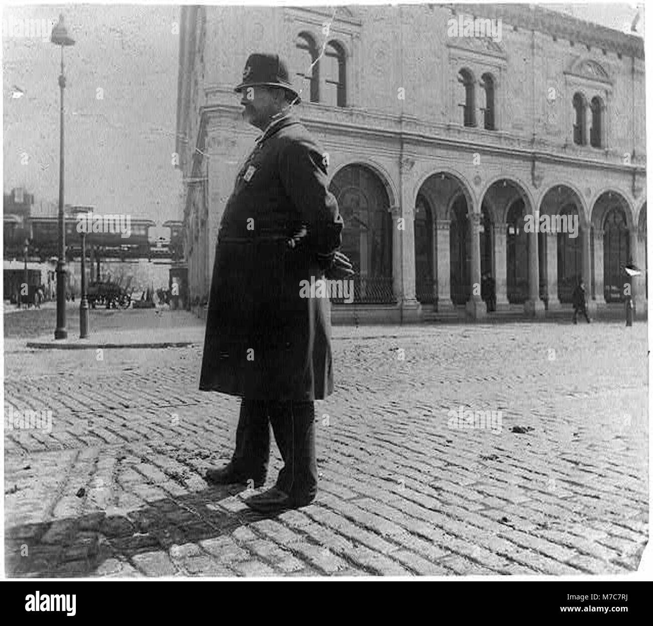 Questa fotografia mostra un ritratto a figura intera di un poliziotto di New York, in piedi e rivolto a sinistra. Cattura una tipica figura urbana di New York all'inizio del XX secolo, che riflette la presenza delle forze dell'ordine della città. Foto Stock