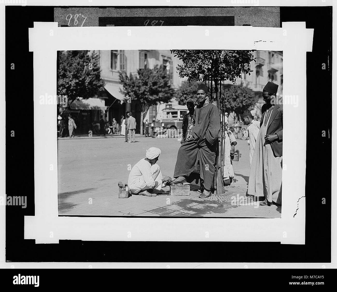 Una scarpa nera al Cairo, possibilmente con un abbigliamento tradizionale, è raffigurata insieme a personaggi egiziani. Questa immagine mostra aspetti della vita quotidiana e dei ruoli sociali in Egitto durante la fine del XIX secolo o l'inizio del XX secolo. Foto Stock