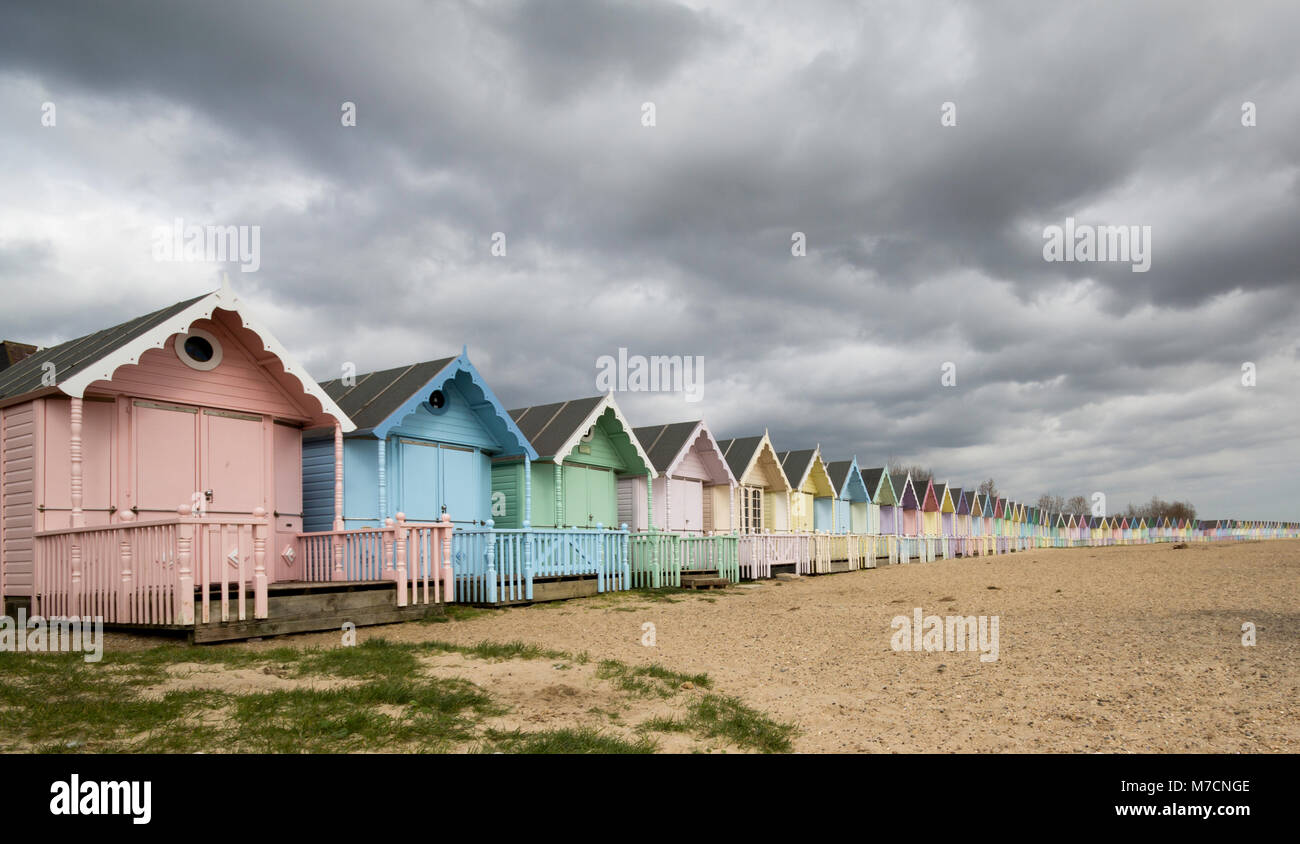 Il pastello colorato capanne sulla spiaggia a East Mersea, Essex con una drammatica cloudscape sopra. Foto Stock