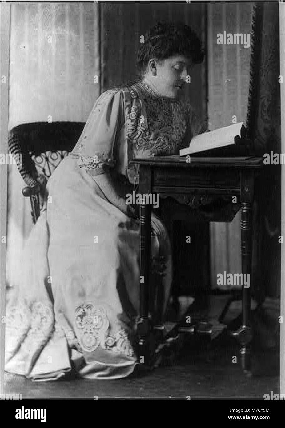 Un ritratto a figura intera di Frances Hodgson Burnett, un'acclamata autrice, seduta a un tavolo a leggere. L'immagine cattura il suo atteggiamento ponderato e ponderato. Foto Stock