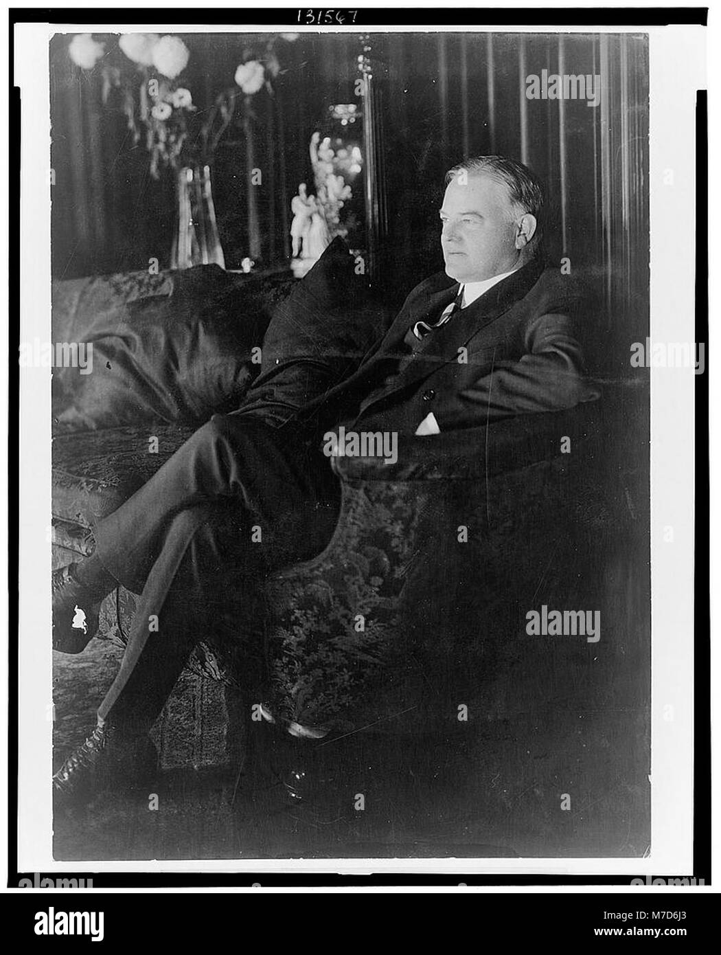Un ritratto a figura intera di Herbert Hoover, il 31° Presidente degli Stati Uniti, seduto su un divano e rivolto a sinistra. L'immagine cattura il comportamento formale di Hoover durante il suo mandato. Foto Stock