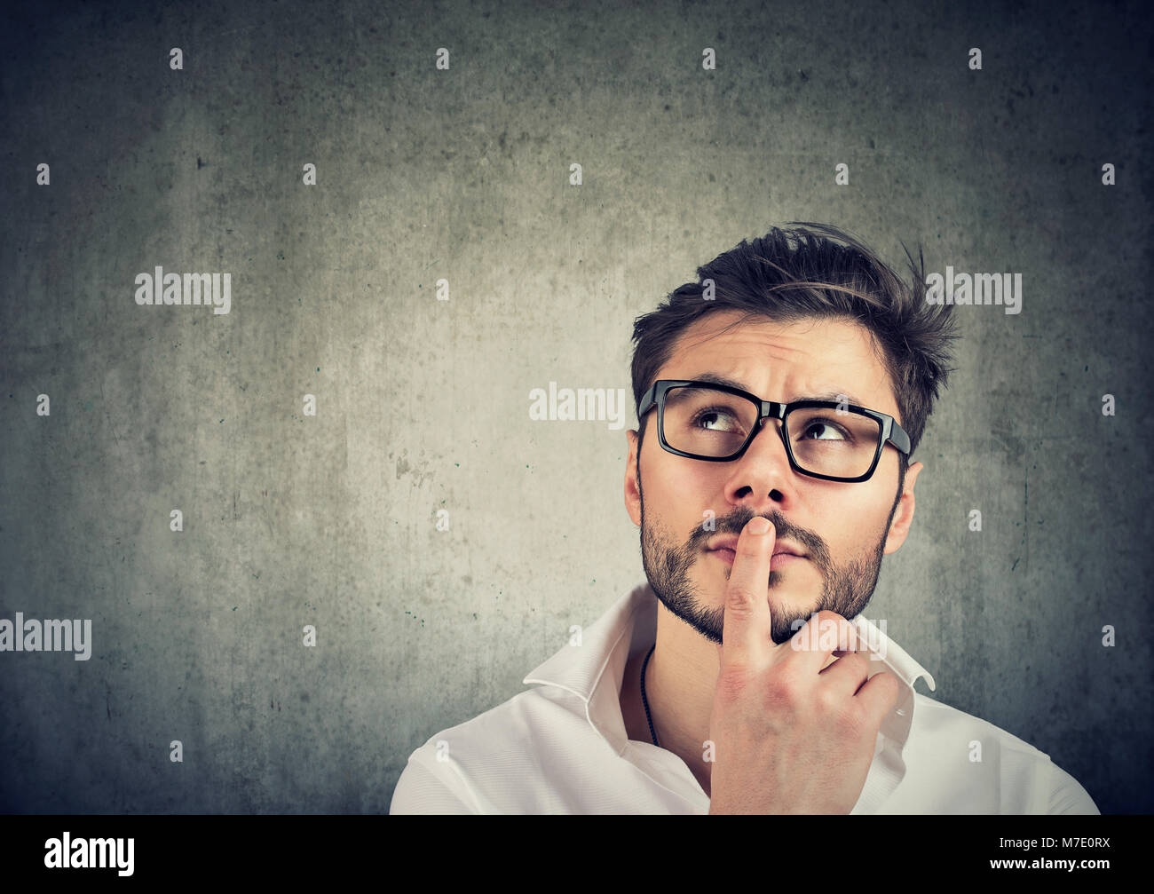 Giovane uomo bello in bicchieri di pensare in dubbi e toccando le labbra sul grigio. Foto Stock