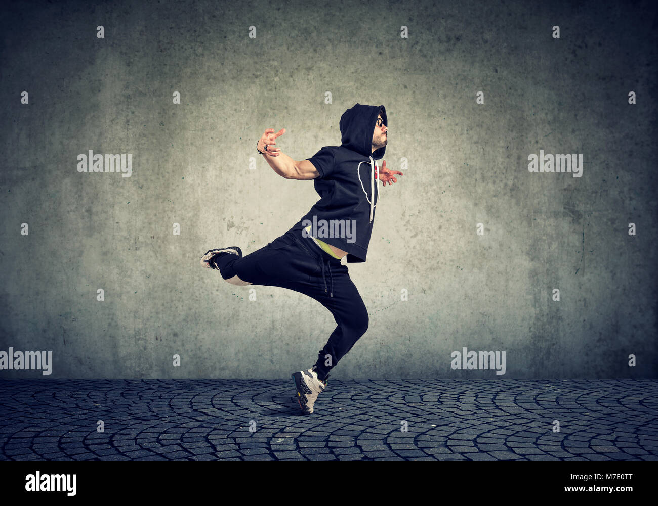 Elegante giovane uomo nel quartiere alla moda di abbigliamento sportivo di eseguire street dance con sul muro grigio Sfondo. Foto Stock