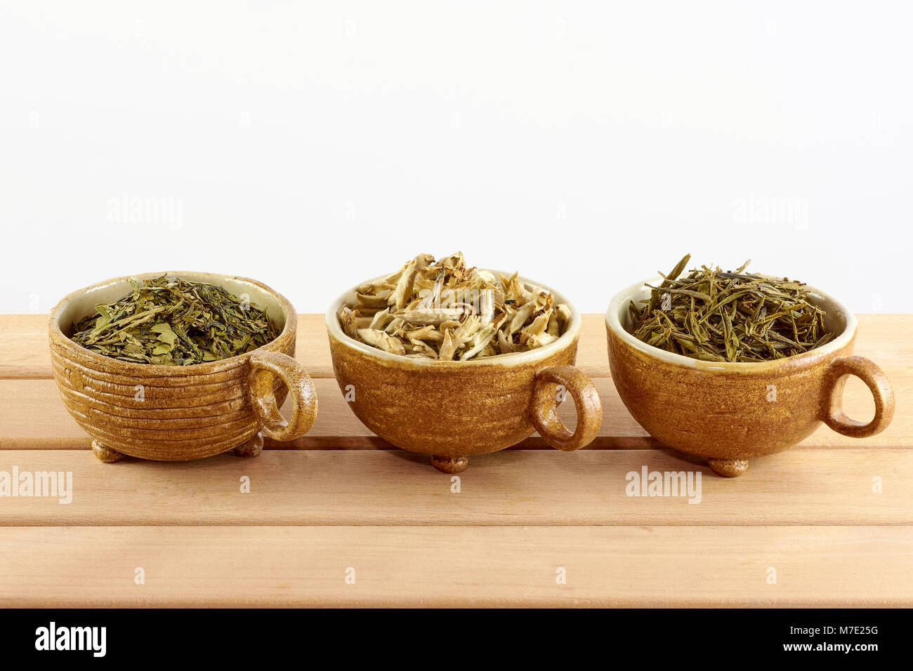 Tre tazze con verde bianco e le foglie di tè su sfondo bianco Foto Stock