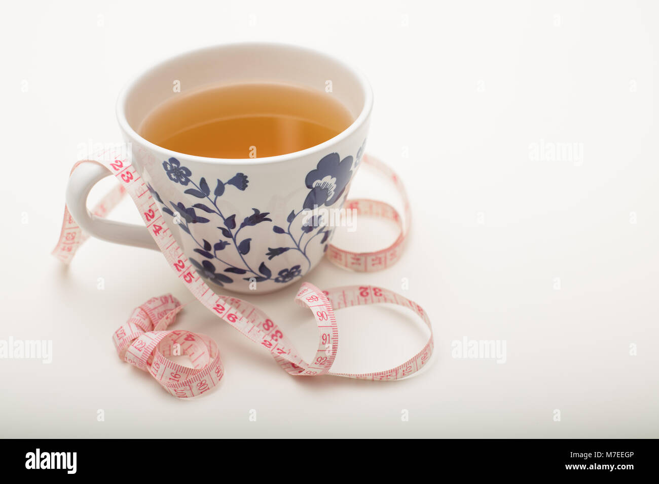 Tazza di acqua calda tè nero con nastro di misurazione su uno sfondo bianco con copia spazio in un concetto di perdita di peso e di una dieta sana Foto Stock