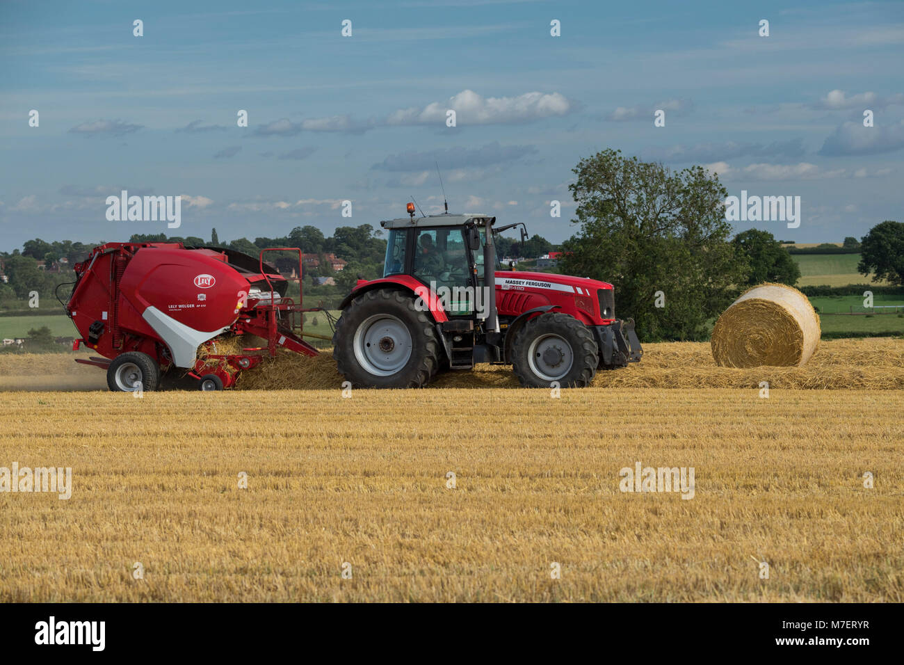 Le balle di paglia in una fattoria campo, un agricoltore lavora e unità trattore rosso tirando la rotopressa & passando grandi balle - Whixley, North Yorkshire, Inghilterra, Regno Unito. Foto Stock