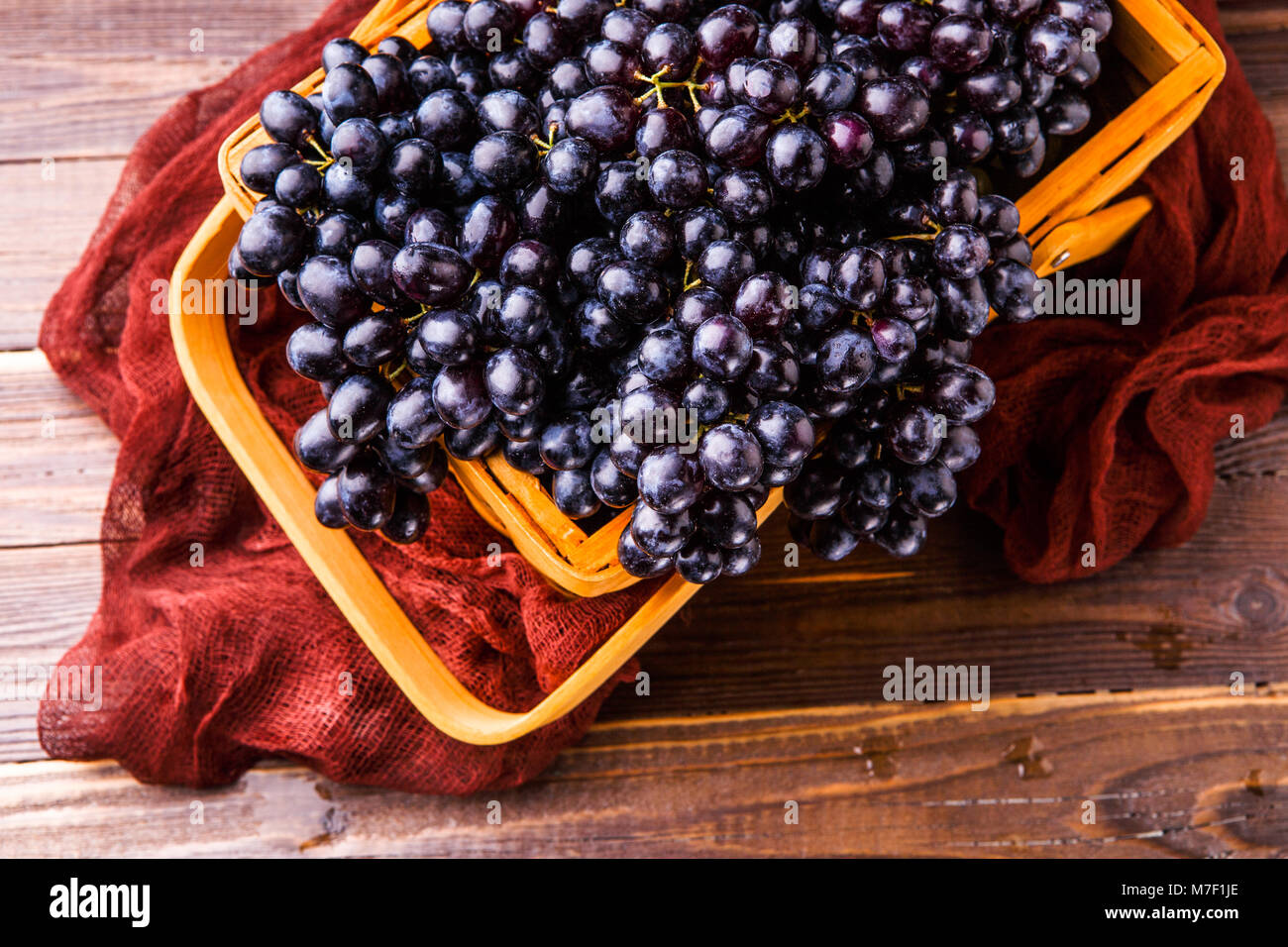 Immagine da sopra di uve nere nel cesto in legno con panno claret Foto Stock