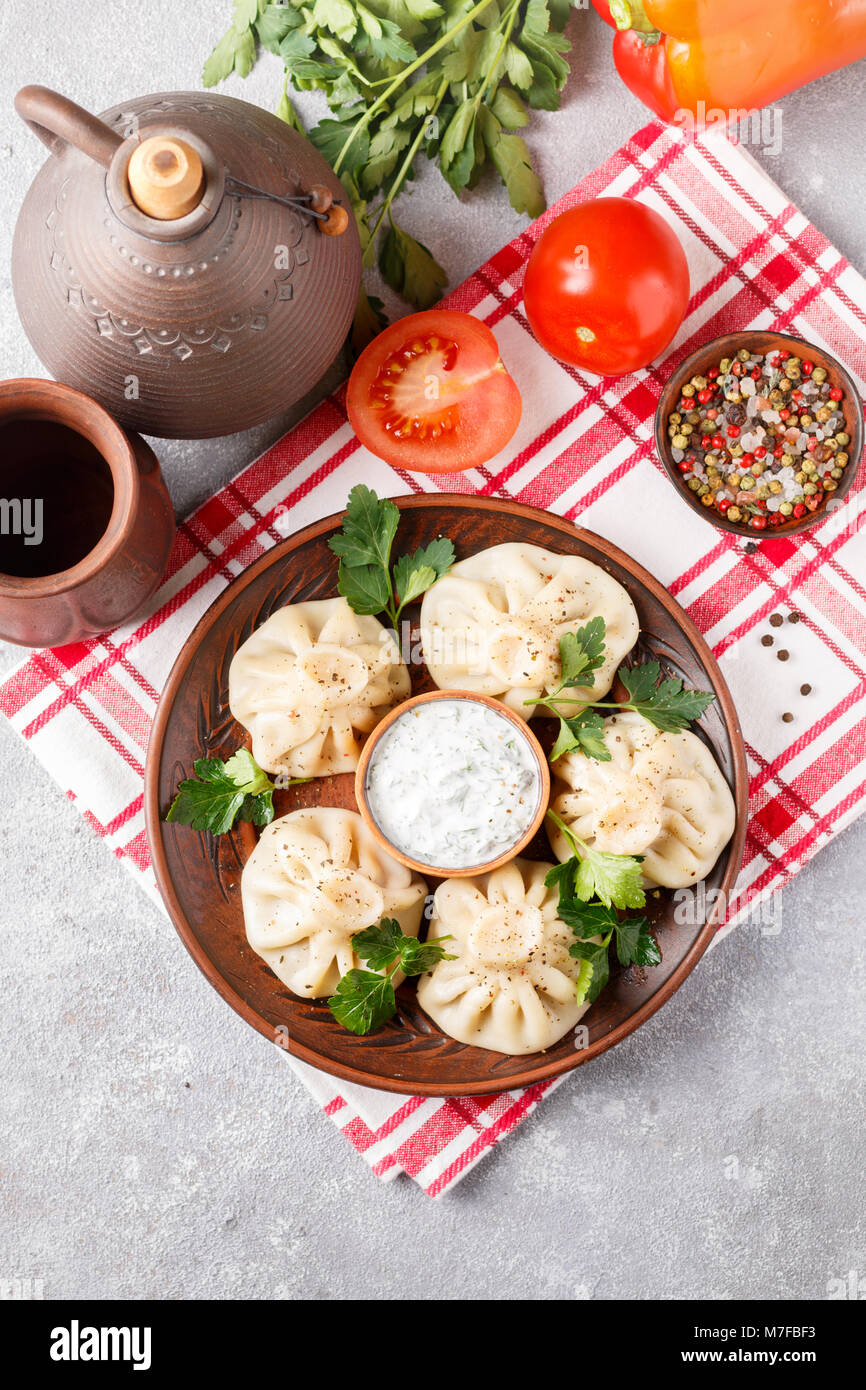Khinkali - Georgian gnocchi con carne e prezzemolo in un piatto di ceramica con una salsa di panna acida e verdi. Messa a fuoco selettiva. Vista superiore Foto Stock