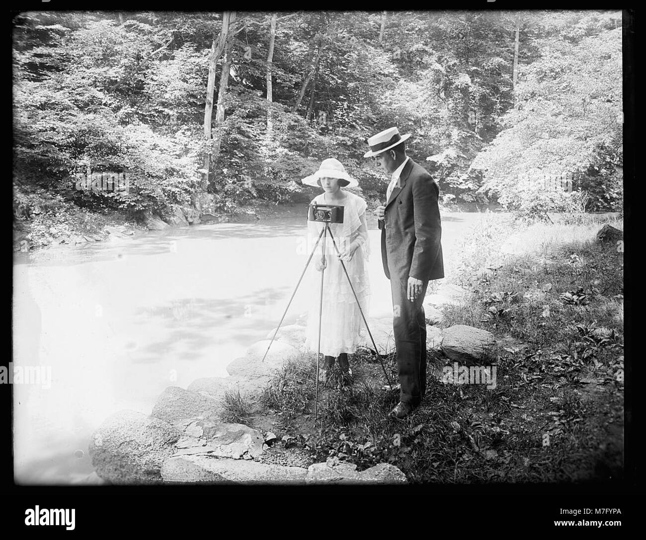 Questa immagine raffigura una donna con una macchina fotografica e un uomo in un ambiente boscoso, forse catturando la natura o i momenti all'aperto. Riflette un momento nella natura, sottolineando un legame con l'ambiente. Foto Stock