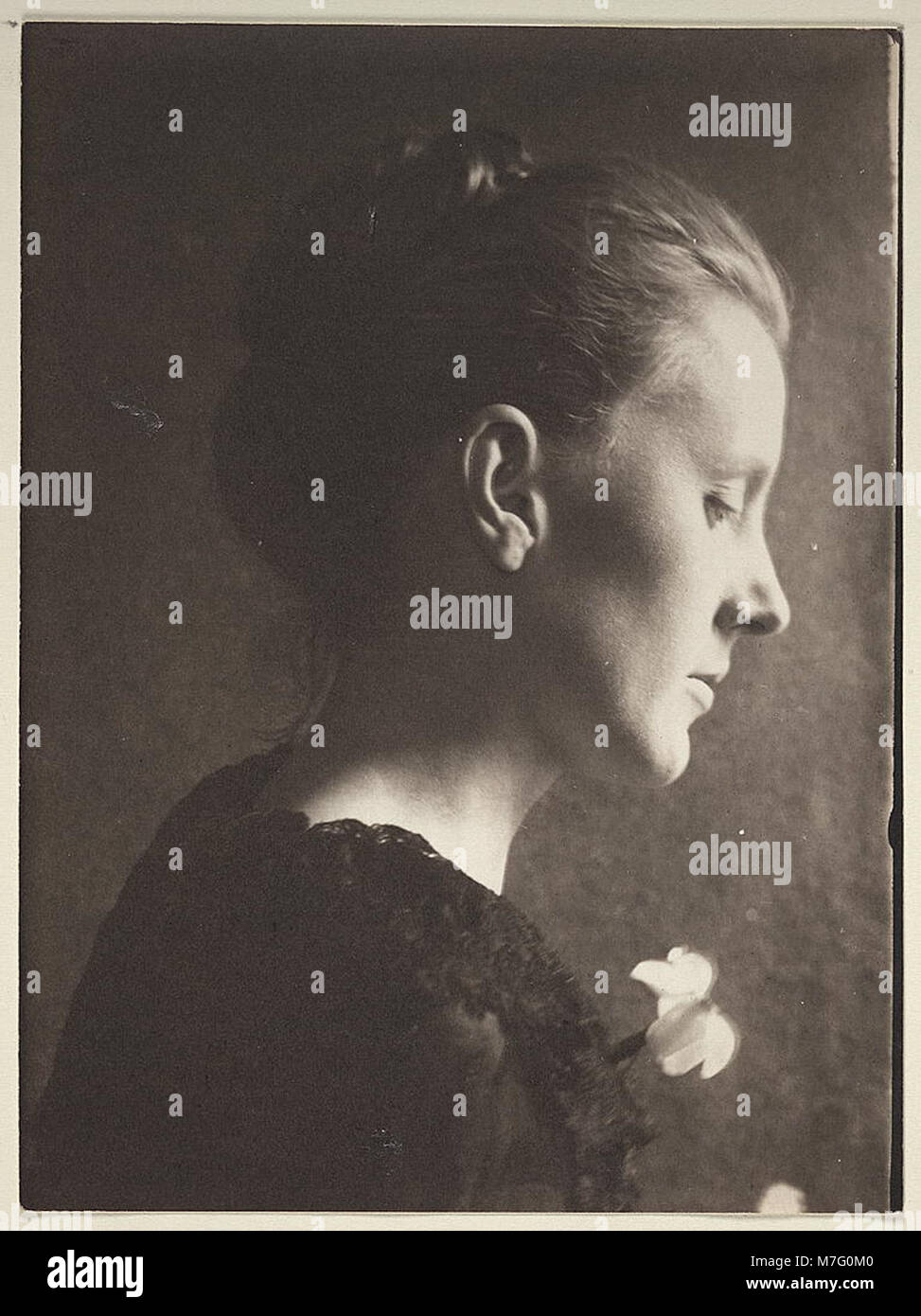 Un ritratto di profilo di una giovane donna vestita di nero con un fiore nei capelli. L'immagine cattura l'eleganza e lo stile della moda dei primi anni del XX secolo. Foto Stock