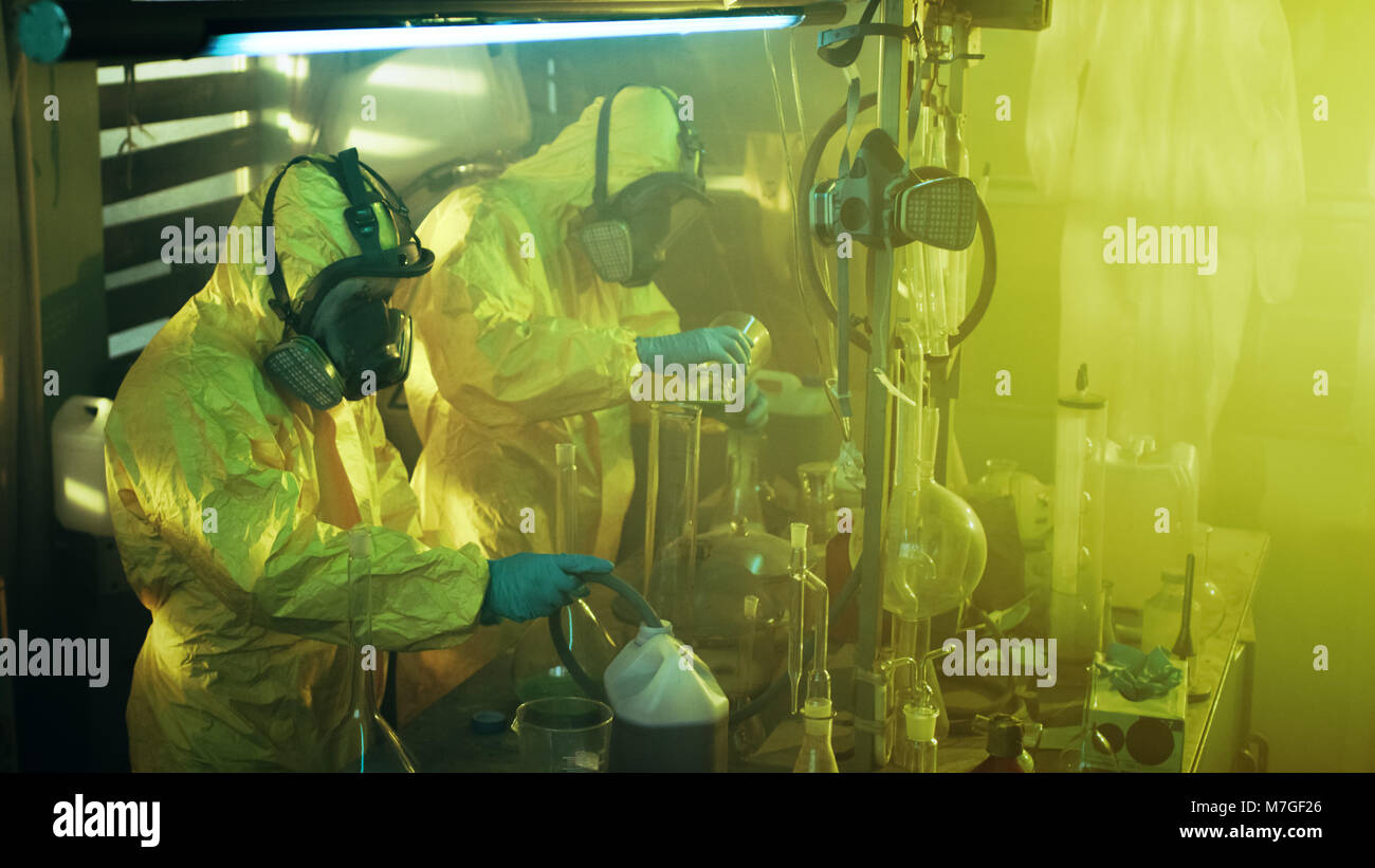 Nel laboratorio sotterraneo due chimici clandestino indossando tute protettive e maschere cuocere la droga. Essi lavorano con bicchieri, distillazione. Foto Stock