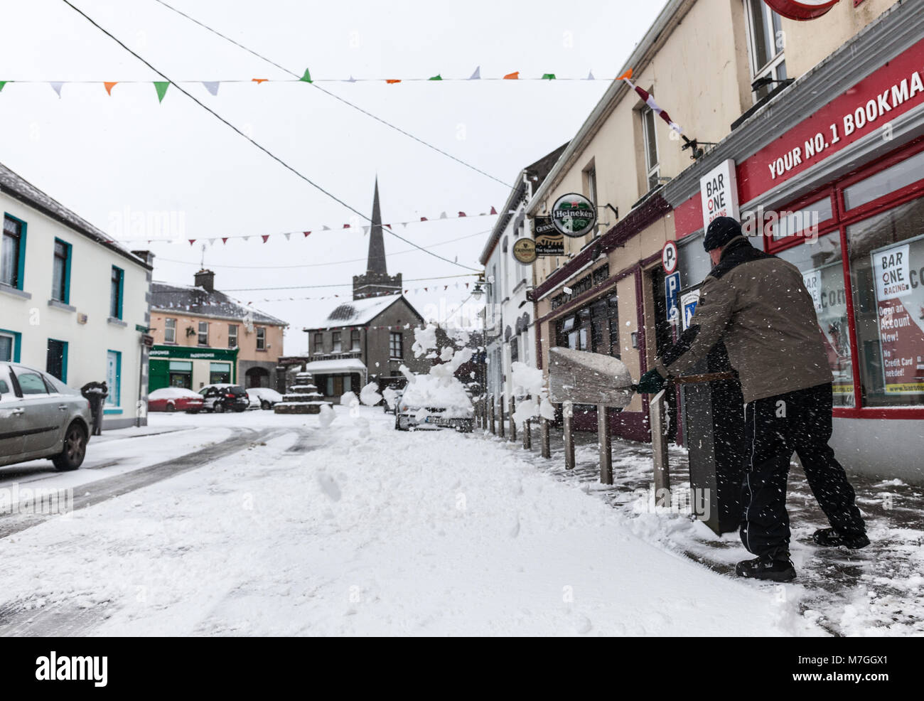 ATHENRY, Irlanda - MARZO 02: uomo non identificato un raschiamento neve a fronte della piazza Inn pub durante la tempesta Emma su Marzo 02, 2018 in Athenry, IRELA Foto Stock