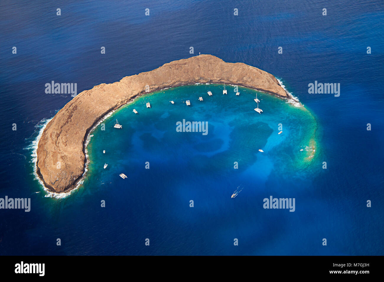 Molokini cratere, antenna colpo di forma di una mezzaluna isolotto a metà mattina con barche a noleggio, Maui, Hawaii. Foto Stock