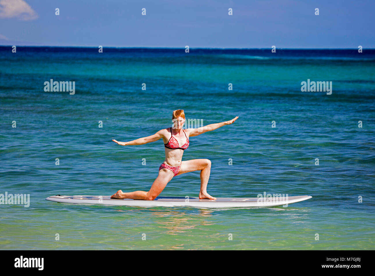 Una donna su uno stand up paddle board in una posizione di yoga, Maui, Hawaii. Foto Stock