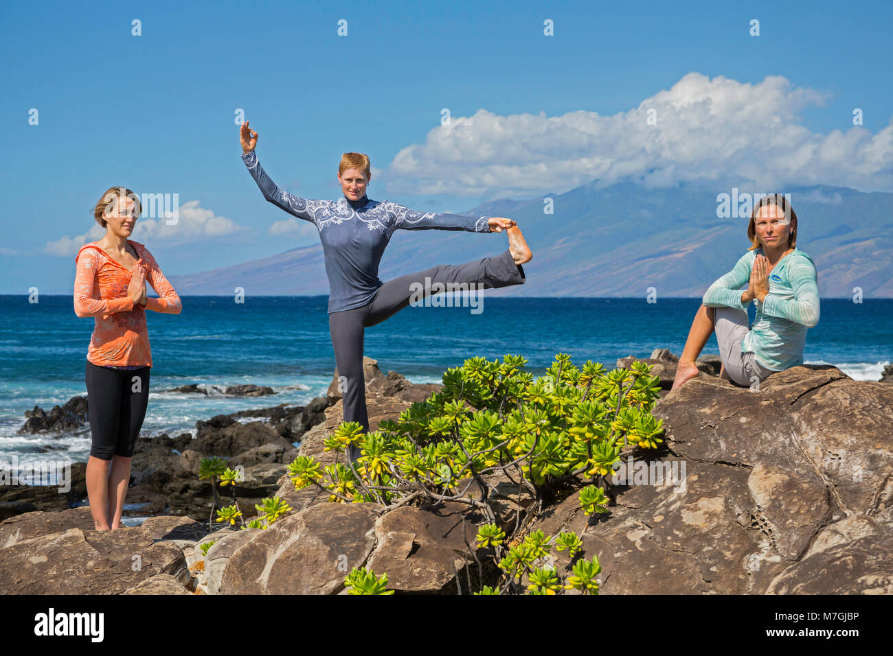 Tre donne (MR) davanti all'oceano in posizioni di yoga, Kapalua Bay, Maui, Hawaii, Stati Uniti d'America. Foto Stock