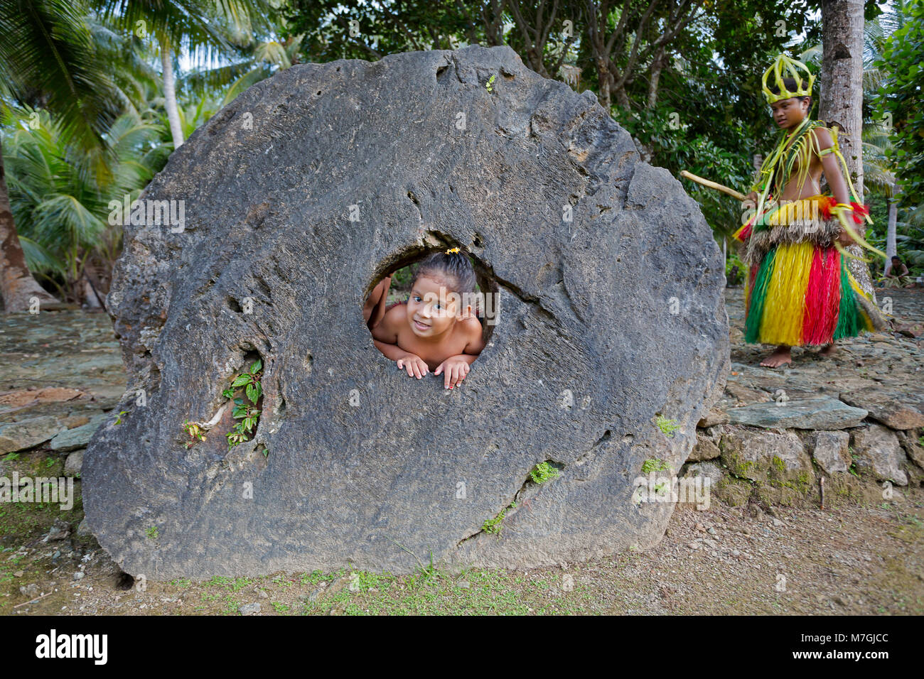 Questa ragazza è raffigurato guardando attraverso il foro nel centro di pietra del denaro in un villaggio sull'isola di Yap, Micronesia. Foto Stock