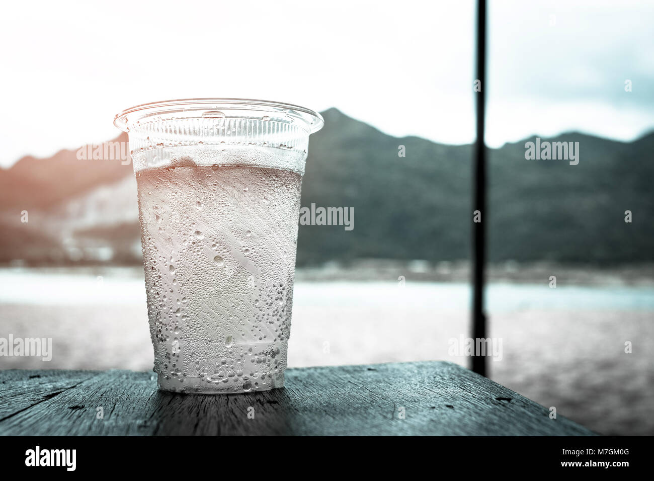 Un bicchiere di plastica di acqua sul tavolo di legno sulla spiaggia in estate. La luce del sole splendente al vetro e di gocce di acqua condensata fuori del vetro Foto Stock