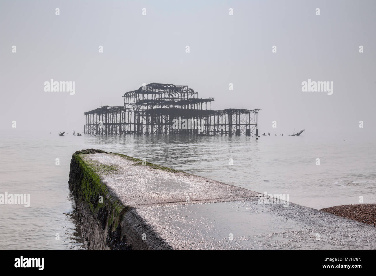 La spiaggia di Brighton e i resti del vecchio molo Ovest su un nebbioso giorno in luce piatta, Sussex, Inghilterra, Regno Unito. Foto Stock