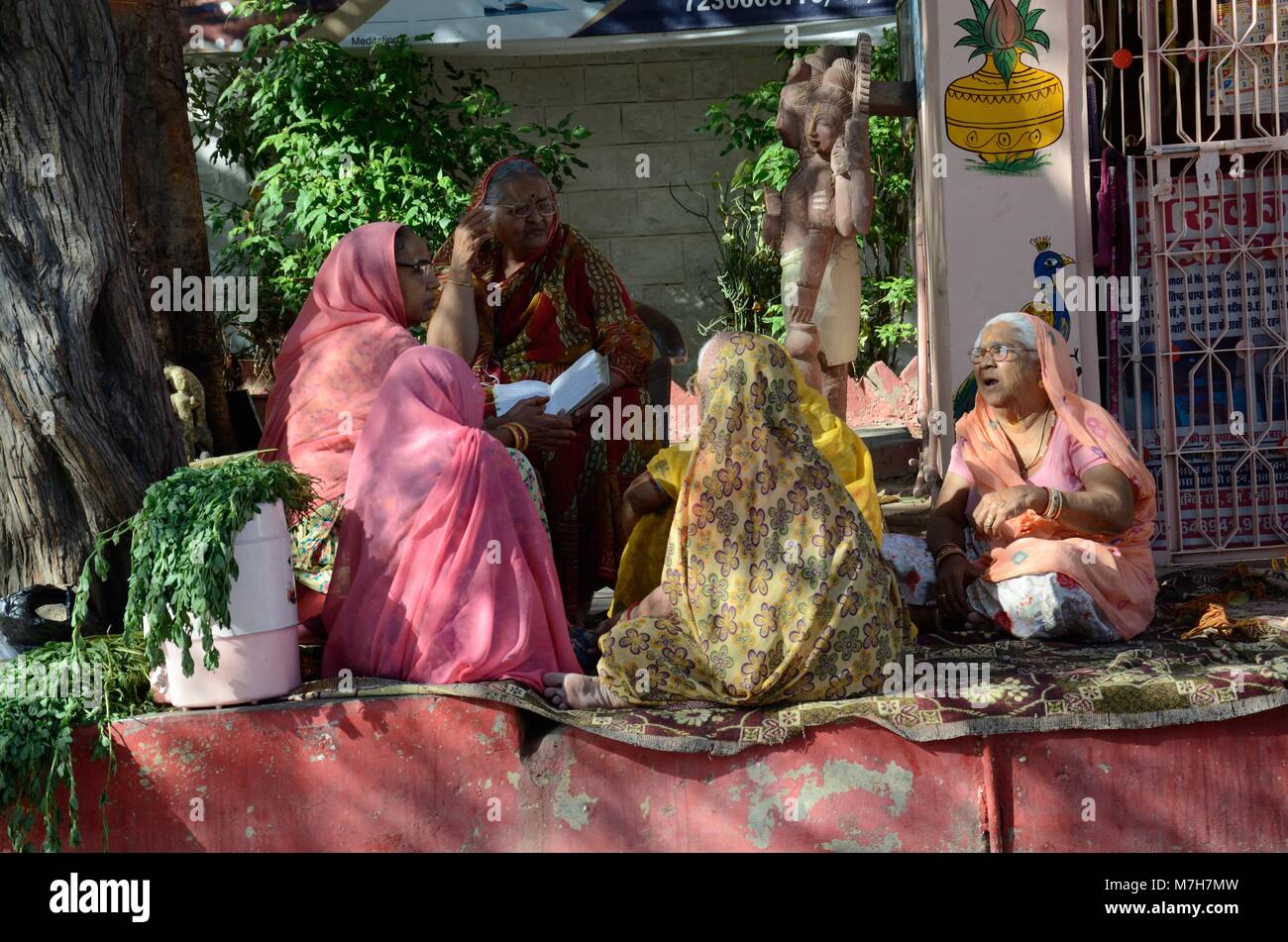 Un gruppo di Indiani senior donne che indossano sari colorati seduto sotto un albero in un tempio indù di cantare bhajan Udaipur Rajasthan in India Foto Stock