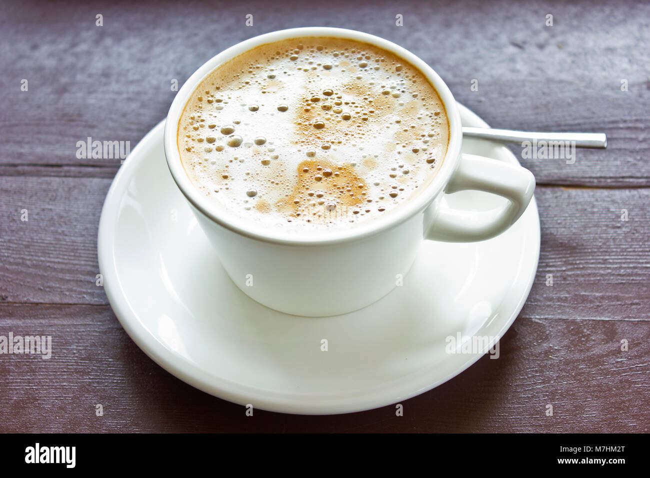 Accessori per caffè cappuccino con schiuma di latte e bolle in un bianco  tazza di porcellana sul piattino in legno marrone a tavola Foto stock -  Alamy