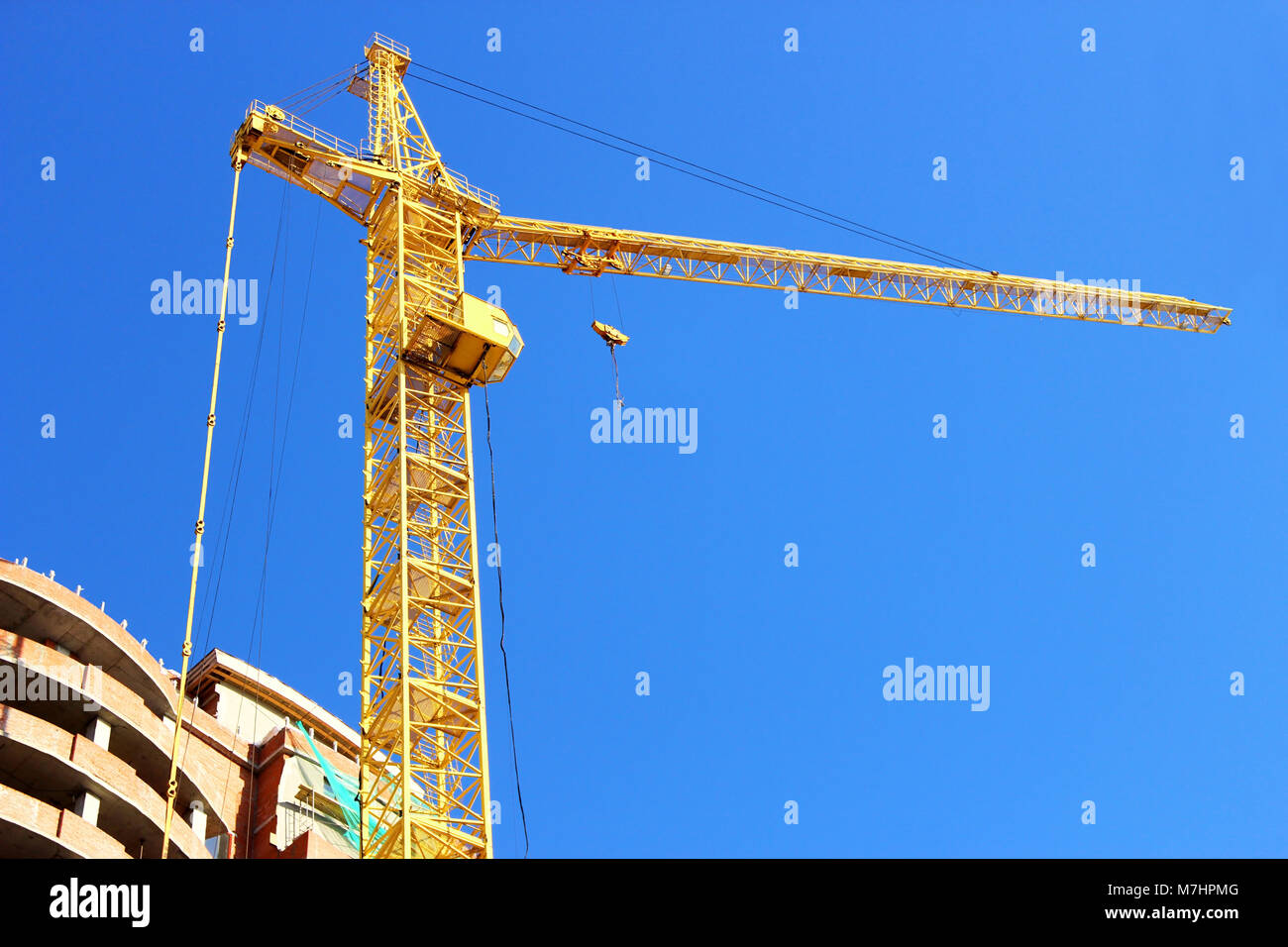Alto edificio di gru da cantiere vicino alla casa in costruzione su uno sfondo di cielo blu. Foto Stock
