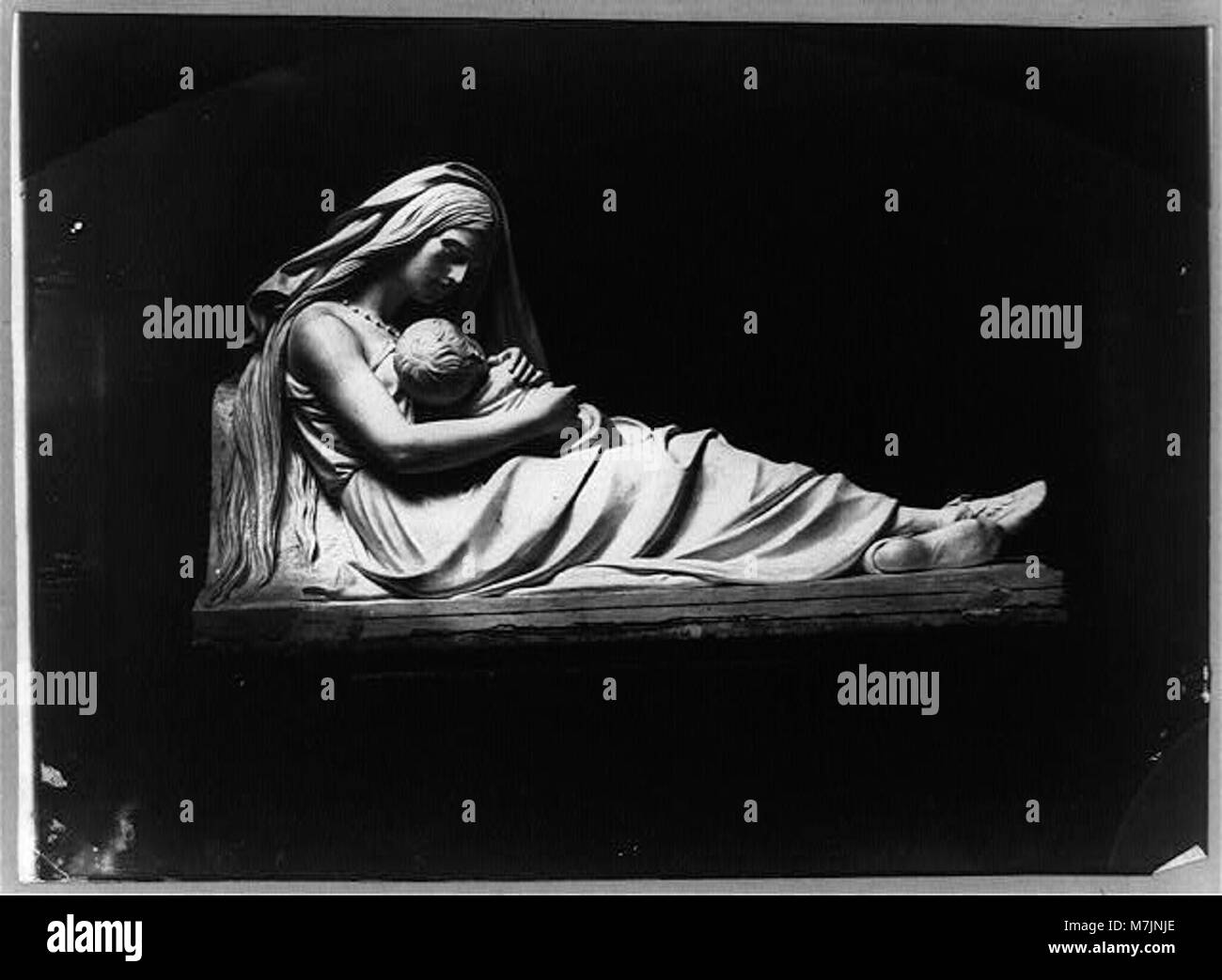 Una scultura raffigurante una donna sdraiata che tiene un bambino tra le braccia, catturata in una forma artistica classica. Questo pezzo rappresenta temi materni nell'arte. Foto Stock