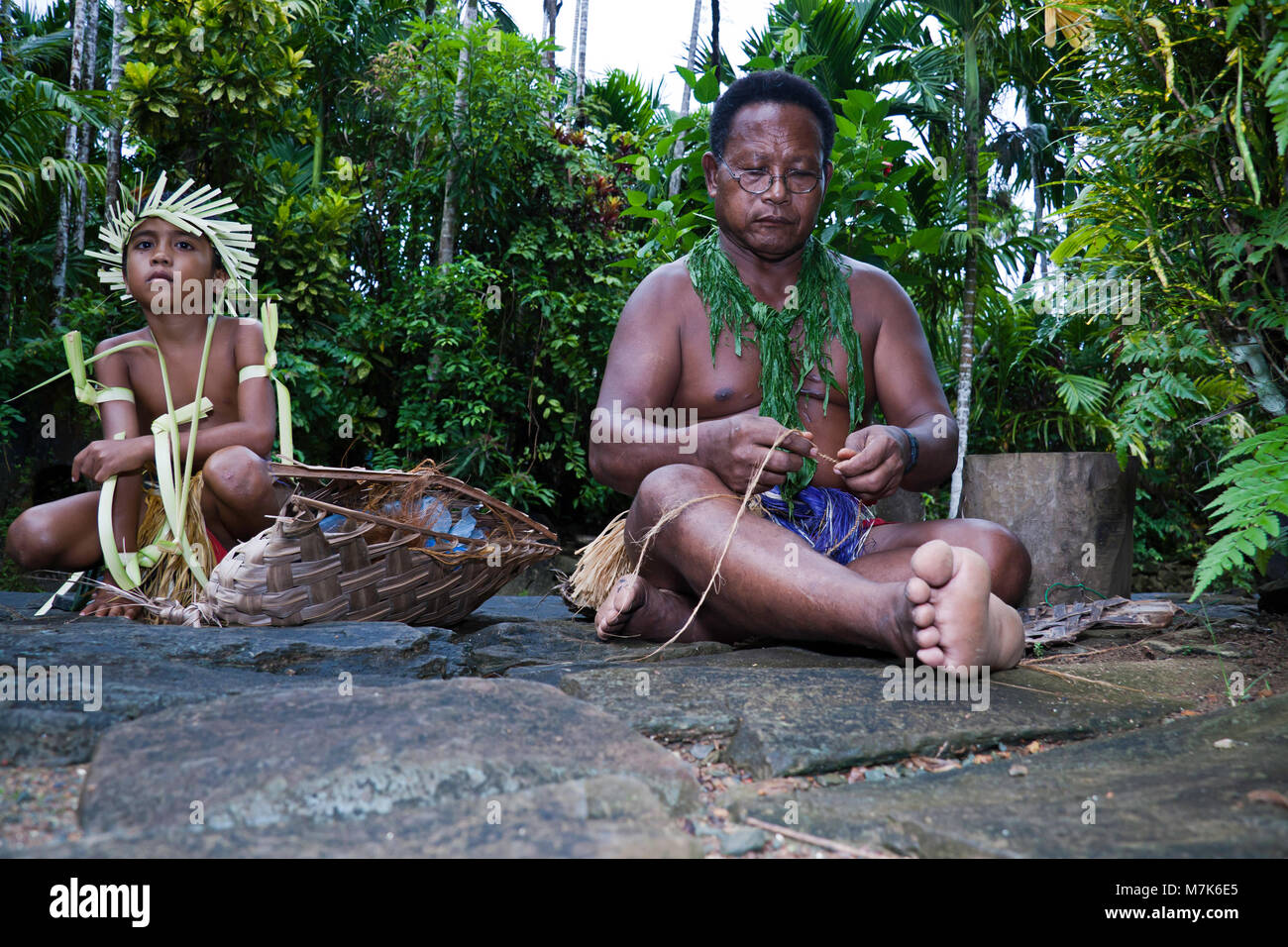 Un uomo e il giovane ragazzo in abito tradizionale. L'uomo è la tessitura fune dalla buccia di cocco sull isola di Yap, Micronesia. Foto Stock