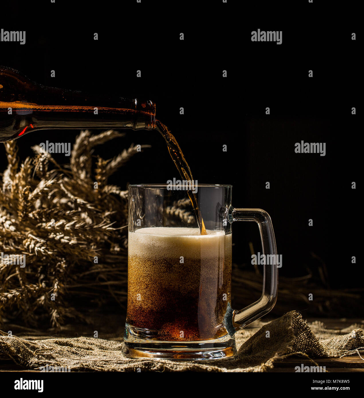 Birra schiumosa versata nella tazza in piedi sul vuoto sullo sfondo di legno Foto Stock