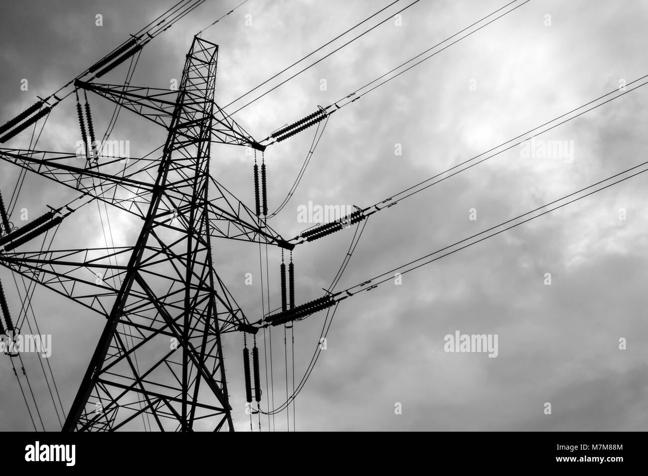Immagine in bianco e nero di un torreggiante pilone di elettricità e linee di alimentazione stagliano contro un cielo nuvoloso Foto Stock