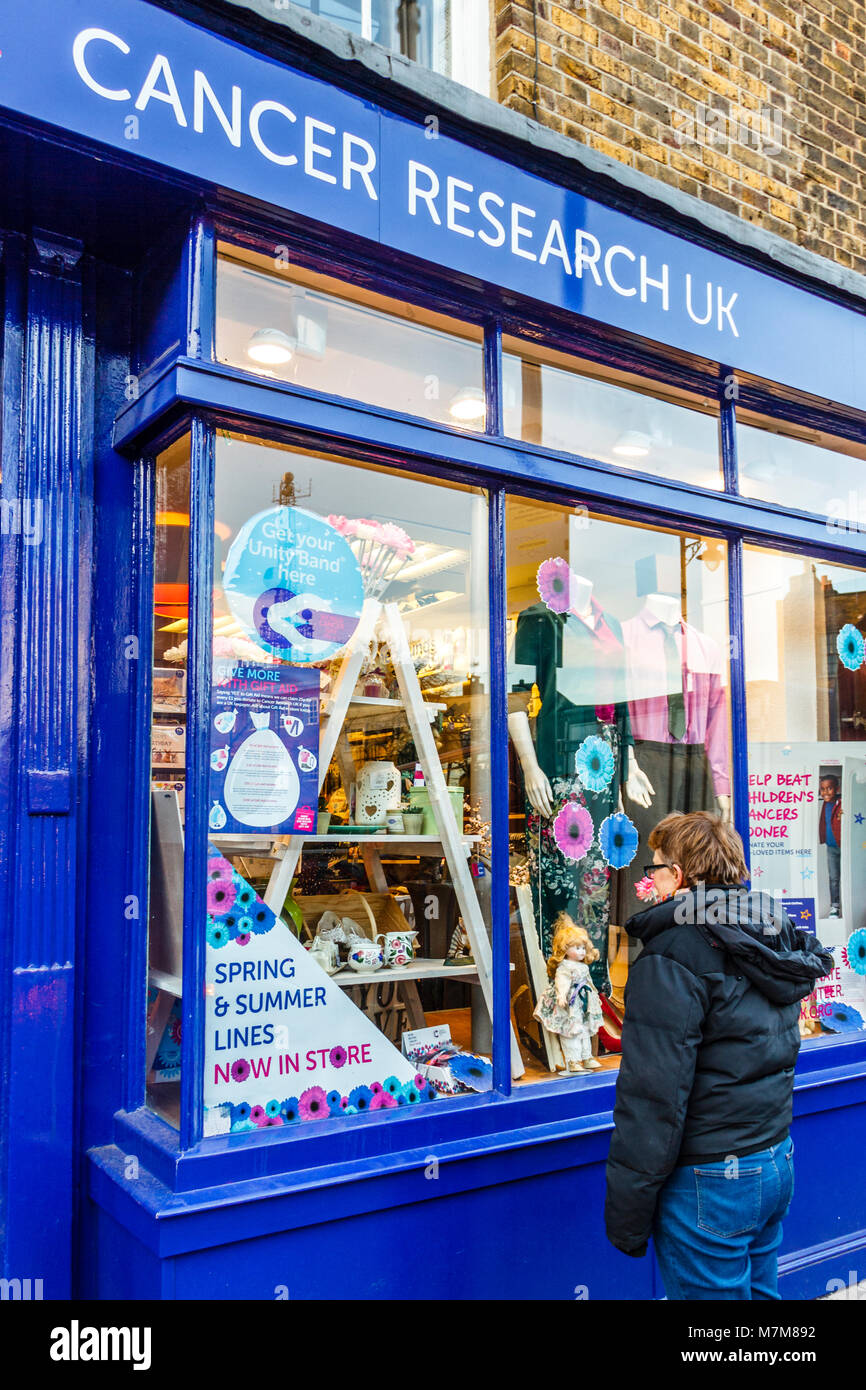 Una donna che guarda nella finestra di un cancro ricerca negozio di carità nel villaggio di Highgate, London, Regno Unito Foto Stock