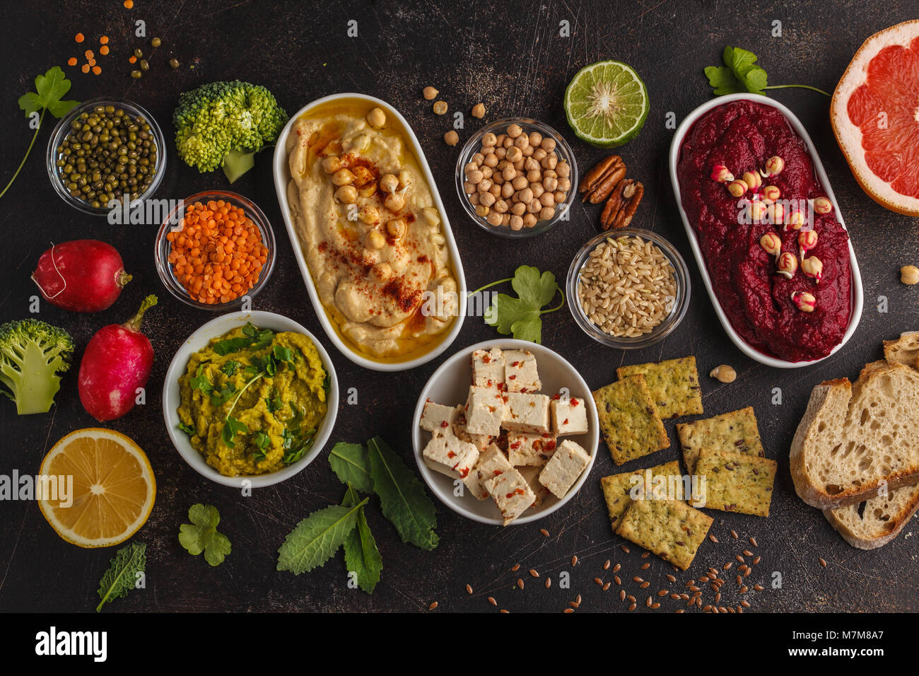 Cibo Vegan sfondo. Spuntini vegetariani: hummus, barbabietole hummus, piselli verdi dip, verdure, tofu. Vista superiore, sfondo scuro, copia dello spazio. Foto Stock