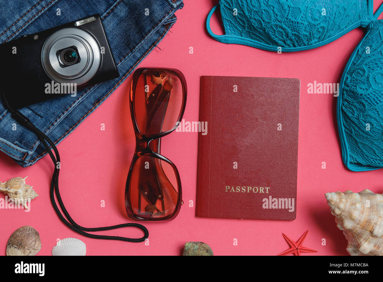 Passaporto, costume da bagno, Jeans, occhiali da sole, fotocamera, il Seashell su sfondo rosa. Vista dall'alto concetto di viaggio. Foto Stock