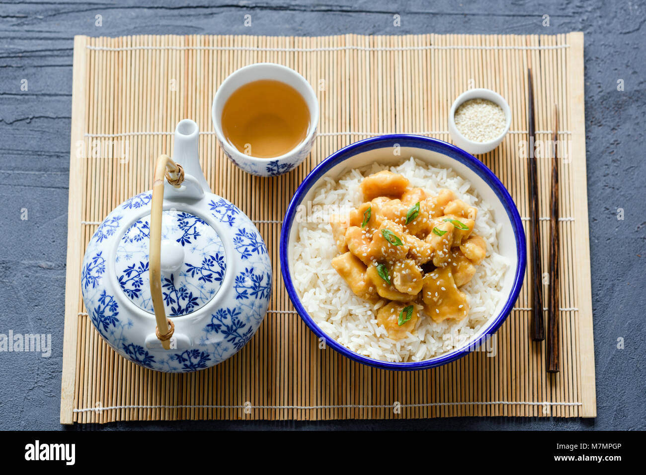 Il cinese pollo con riso, bacchette e tè verde sul foglio di bambù. Tradizionale cucina asiatica Foto Stock