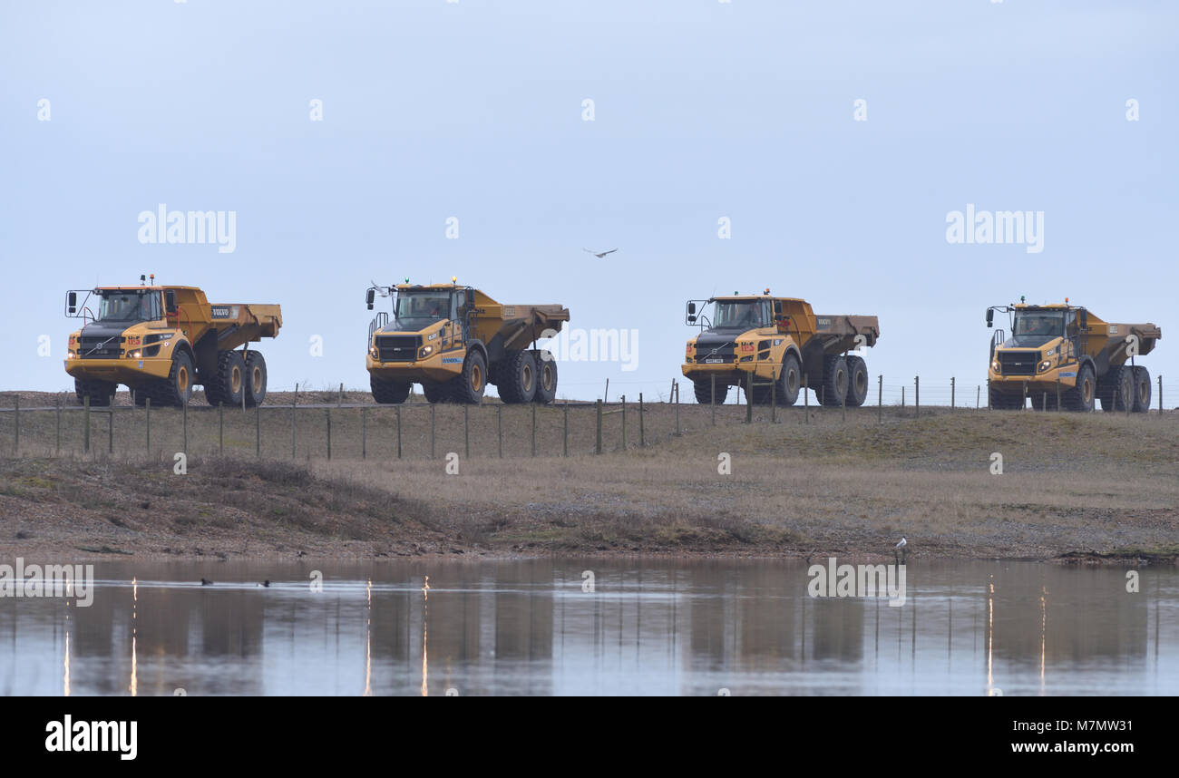 Un convoglio di camion enormi porta shingle dalla foce del fiume Rother verso ovest lungo la costa per sostituire le spiagge erose e proteggere la costa un Foto Stock