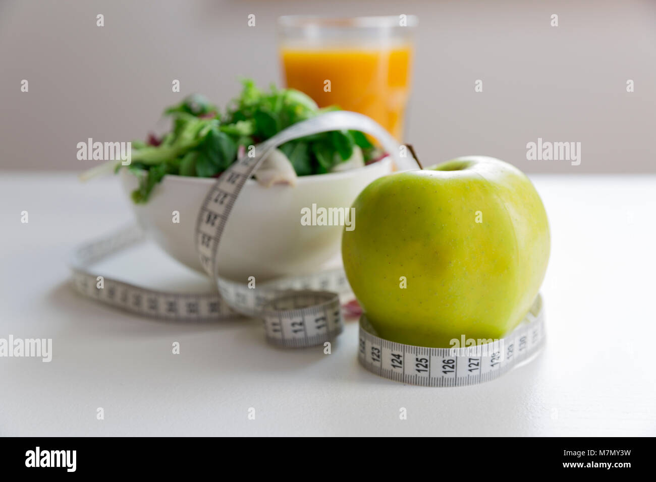 Nastro di misurazione intorno alla Apple, ciotola di insalata verde e bicchiere di succo di frutta. La perdita di peso e il giusto concetto di nutrizione Foto Stock