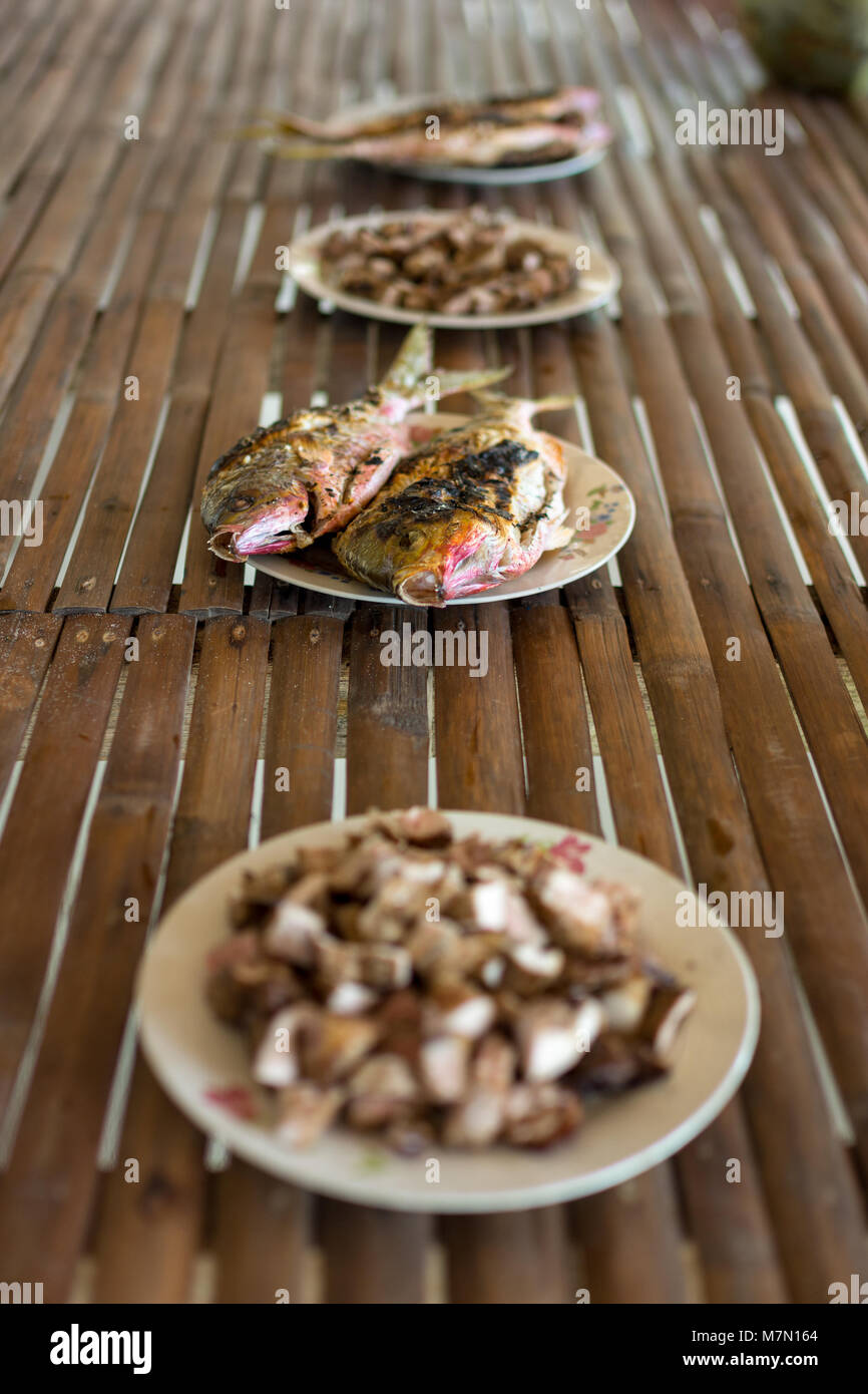 Un semplice appena catturati e pasto cucinato di grigliate di pesce e carne di maiale tagliata a dadini disposto su una base di bambù tavolo. Foto Stock