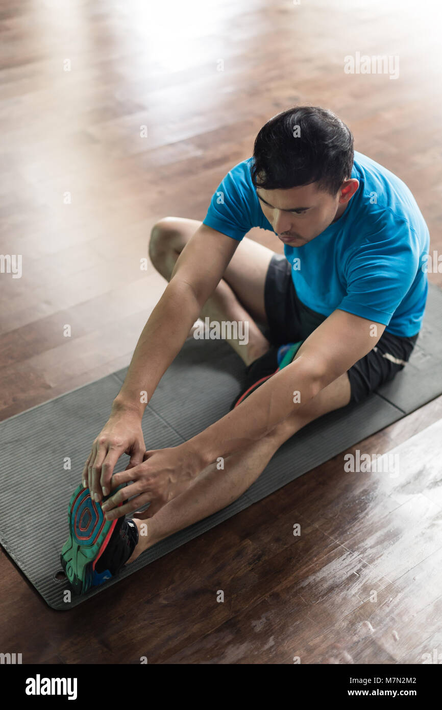 Uomo seduto sul tappeto di esercizio mentre si tocca le sue dita dei piedi Foto Stock