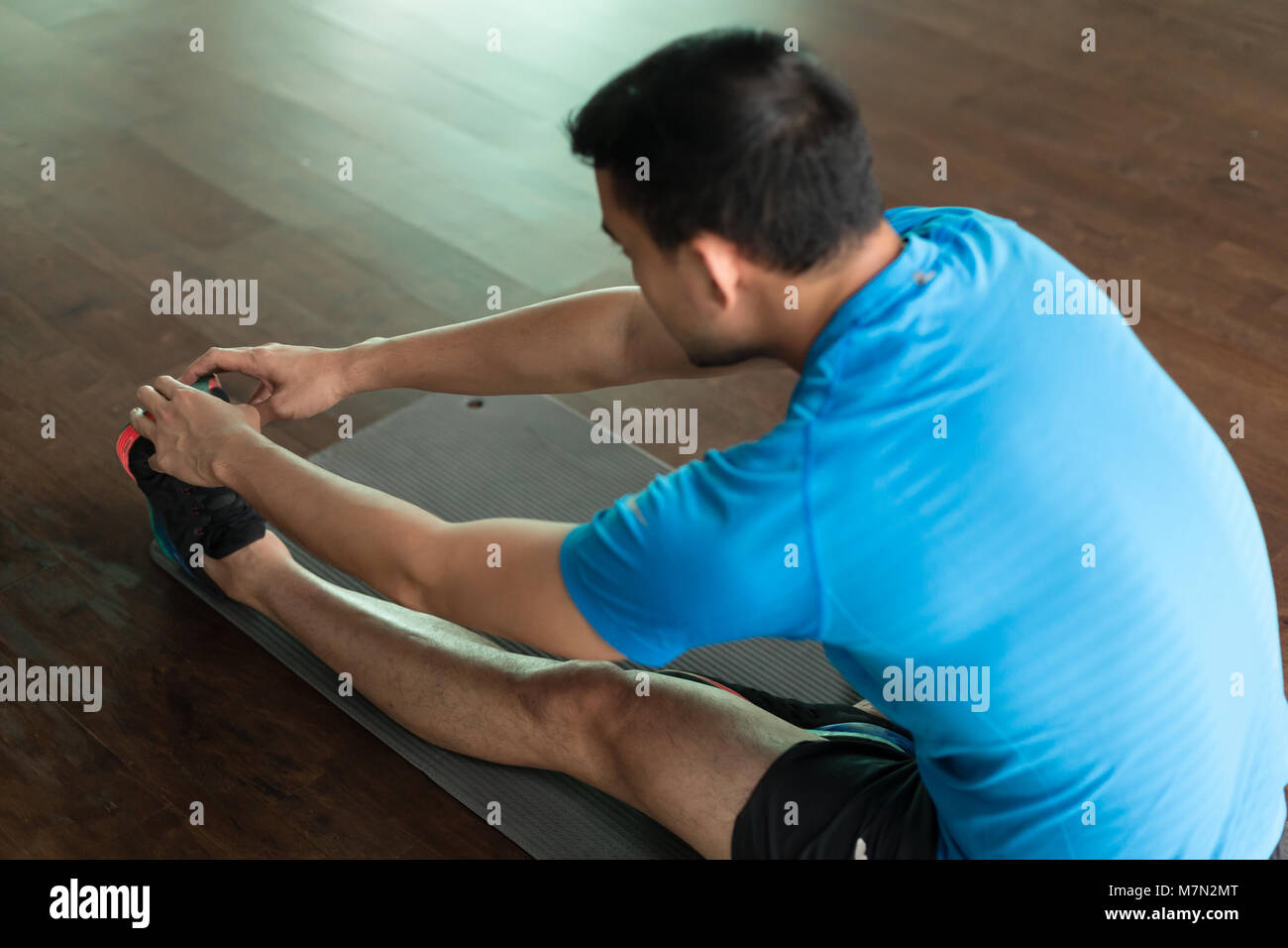 Uomo seduto sul tappeto di esercizio mentre si tocca le sue dita dei piedi Foto Stock