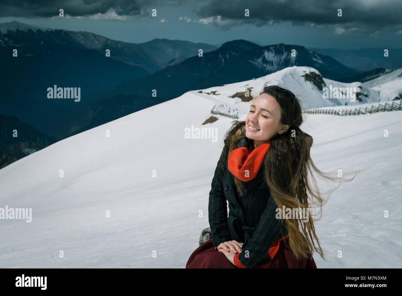 Giovane donna siede sulla cima di montagne innevate in ski resort. Viaggiatori alla moda si gode di una splendida giornata e prende a prendere il sole. Foto Stock