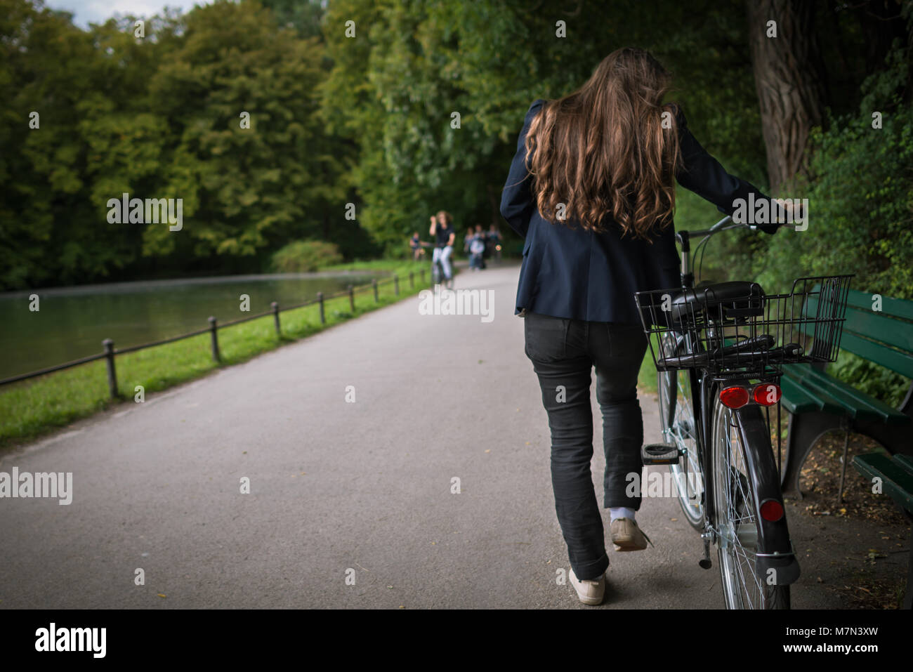 Vista posteriore della giovane donna con la bicicletta nel parco sullo sfondo di alberi e acqua. Attivo alla moda ragazza trascorre del tempo sulla natura Foto Stock