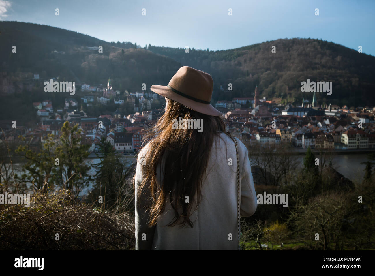 Irriconoscibile la giovane donna in piedi indietro sulla collina e guardando sul paesaggio urbano. Viaggiatori alla moda di prima mattina esplorando parco con splendida vista Foto Stock