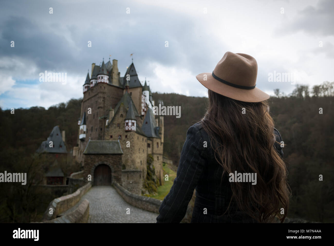 Giovani irriconoscibile donna cammina lungo la strada che conduce a un incredibile castello. Romantico luogo medievale. Raggi di sole cadono sui capelli. Ragazza che viaggiano in Europa Foto Stock