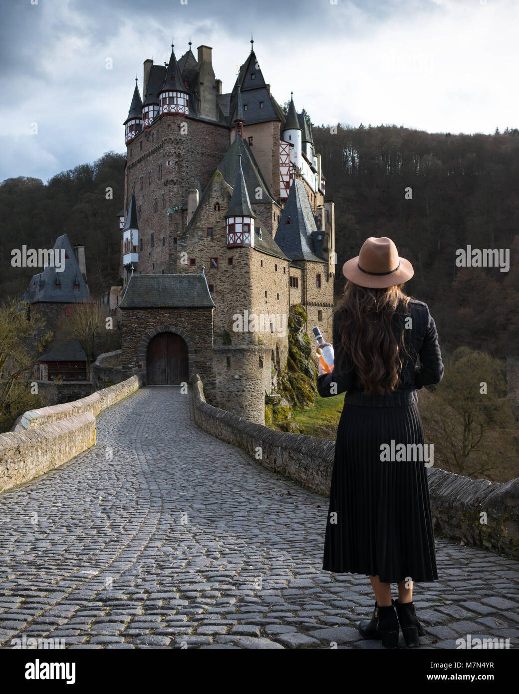 Giovane donna con bottiglia di vino sorge sulla strada che conduce al favoloso castello. Incredibile luogo medievale. Ragazza alla moda si trova a viaggiare in Europa Foto Stock